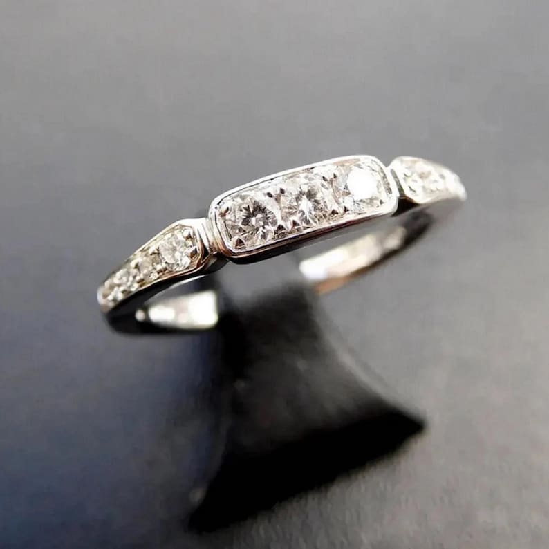 Puede incluir: Un anillo de banda de plata con una fila de peque&ntilde;os diamantes y un diamante rectangular m&aacute;s grande en el centro.