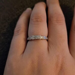 Puede incluir: Un anillo de banda de plata con una fila de peque&ntilde;as piedras transparentes engastadas en forma rectangular.