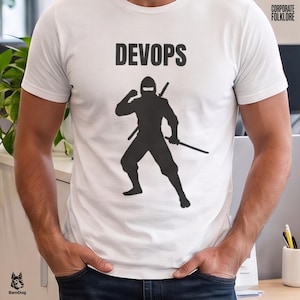 Könnte beinhalten: Ein weißes Kurzarm-T-Shirt mit einer schwarzen Grafik eines Ninjas in Kampfhaltung, der zwei Schwerter hält. Der Text DEVOPS ist in Schwarz über der Ninja-Figur aufgedruckt. Das T-Shirt hat einen Rundhalsausschnitt.