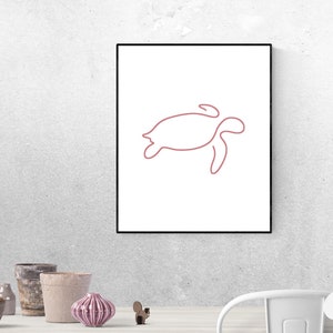 May include: A printable digital download of a line drawing of a sea turtle in a light pink colour. The drawing is framed and hanging on a white wall.
