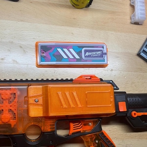 Op de afbeelding: Oranje en zwarte speelgoedpistool met een doorzichtig oranje magazijn en een zwarte handgreep. Het pistool heeft een klein oranje vizier bovenop en een zwarte loop. Het pistool heeft een sticker aan de zijkant met de tekst "Adventure Force".