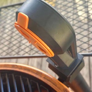 May include: A black and orange digital meat thermometer attached to a grill. The thermometer has a large digital display and a probe that can be inserted into meat to measure its internal temperature.