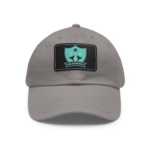 May include: A gray baseball cap with a black patch featuring a white shield with two teal paddleball paddles and a ball. The text "DINK RESPONSIBLY" is printed below the shield.