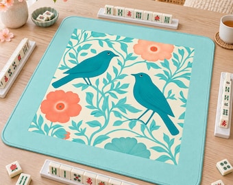 May include: A square mahjong mat with a light blue border and a central cream-colored panel featuring a pattern of two teal birds perched among light blue leafy vines and large peach-colored flowers, surrounded by white mahjong tile racks.