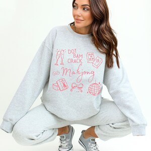 May include: Light gray sweatshirt and sweatpants set with a pink Mahjong graphic. The graphic includes champagne flutes, dice, and a disco ball. The text on the sweatshirt says "Dot Bam Crack Mahjong".