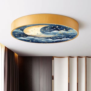 May include: A round ceiling light fixture with a wooden frame. The center features a watercolor design of a crescent moon, stars, and clouds in shades of blue, gold, and white. The fixture is mounted on a white ceiling.