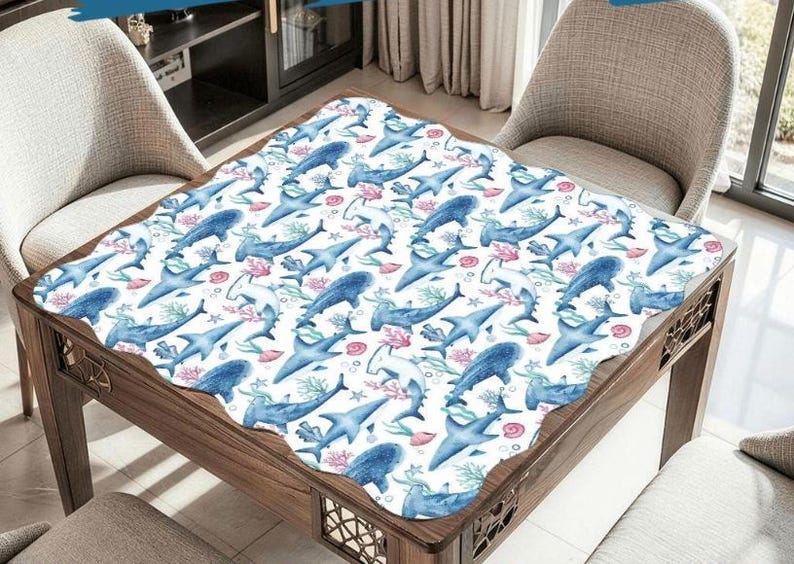 K&ouml;nnte beinhalten: Eine wei&szlig;e Tischdecke mit einem sich wiederholenden Muster aus blauen Haien, Korallen und Seegras. Die Tischdecke liegt auf einem Holztisch mit gewelltem Rand. Die Haie sind in verschiedenen Posen, was ein Unterwassermotiv ergibt.