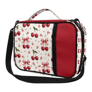 May include: A white and red lunch bag with a black shoulder strap. The bag features a pattern of red cherries with pink bows and flowers. A solid red panel is on the side, and a black zipper runs down the front.