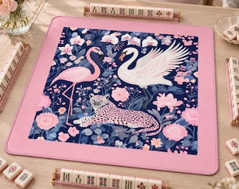 May include: A square mahjong mat with a pink border and a central dark blue field featuring a pink flamingo, a white swan, and a spotted leopard surrounded by pink and white flowers. Four tile racks with mahjong tiles are placed around the mat.