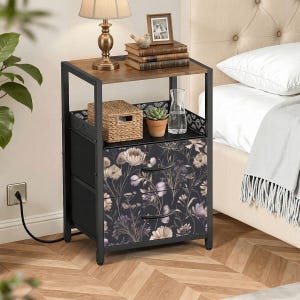 May include: A black and brown nightstand with a floral design on the drawers. The nightstand has a metal frame, a wooden top, and two drawers. A lamp, books, and decorative items sit on top.