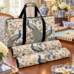 Könnte beinhalten: Eine rechteckige, gesteppte Tragetasche und zwei passende zylindrische Etuis mit einem blau-beigen Pfauen- und Blumenmuster. Die Taschen haben schwarze Stoffgriffe und einen Reißverschluss mit einem sich wiederholenden Vogelmotiv.