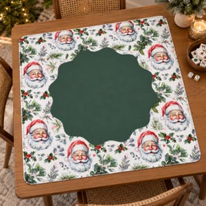 May include: A square fabric mat featuring a repeating pattern of Santa Claus faces, green leaves, and red berries on a white background, with a large, dark green, scalloped-edge shape centered in the middle of the design.