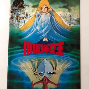 May include: A vintage book cover featuring a woman with long blonde hair and a blue dress. The title "1000 Year Queen" is in red Japanese characters. The artwork has a surreal, dreamlike quality with a mirrored image.