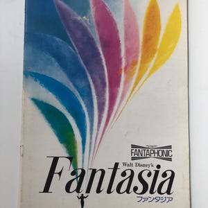 May include: A vintage poster for Walt Disney's Fantasia, featuring a colourful abstract design of rainbow-coloured leaves with a fairy flying in the centre. The poster is titled "Fantasia" in bold black letters with the text "Walt Disney's" above it and "ファンタジア" (Fantasia in Japanese) below it. The poster also includes the text "Fantasophonic" in a black rectangle.