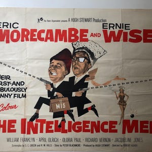 以下が含まれることがあります： エリック・モアカムとアーニー・ワイズ主演の映画「インテリジェンス・メン」のヴィンテージ映画ポスター。ポスターは赤と白の配色で、変装した2人のコメディアンの白黒写真が掲載されている。ポスターには「Their First-and Fabulously Funny Film in Colour」というテキストが書かれている。