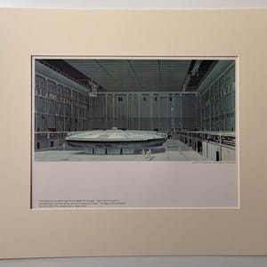 Puede incluir: Una impresión enmarcada que representa una ilustración detallada de una gran nave espacial circular dentro de un hangar. La obra de arte se encuentra en un gran espacio abierto con arquitectura industrial. La impresión está enmarcada en un color neutro.