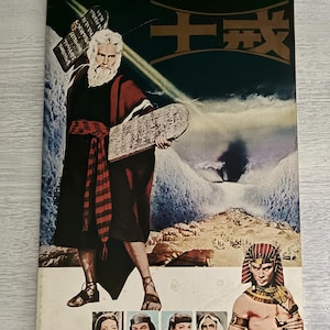 May include: Aged vintage movie poster with a central figure in a robe, holding stone tablets. The poster features Japanese text and images of other characters. The background is dark, and the poster shows signs of wear and age.