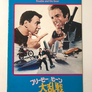 May include: A vintage movie poster for "Freebie and the Bean" featuring Alan Arkin and James Caan. The poster has a blue border and includes action scenes with cars, motorcycles, and a cityscape background. Japanese text is also present.