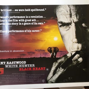 Op de afbeelding: Filmposter voor "White Hunter Black Heart" met Clint Eastwood. De poster toont het gezicht van Eastwood, met een zonsondergang en een olifant op de achtergrond. Tekst bevat citaten en filmcredits.