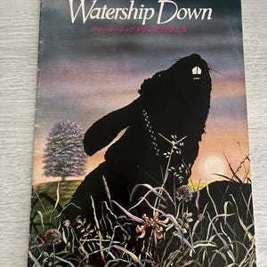 May include: A book cover for "Watership Down" featuring a black silhouette of a rabbit against a sunset backdrop. The title is in white, with Japanese text below. The scene includes tall grass and a tree.