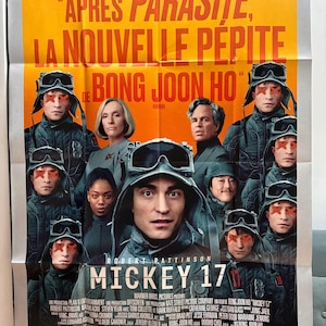 Peut inclure: Affiche du film "Mickey 17" de Bong Joon-ho, avec Robert Pattinson. L'affiche présente un fond jaune et orange avec le titre du film et les acteurs. Les acteurs portent des uniformes sombres et des lunettes, avec des marques rouges sur le visage.