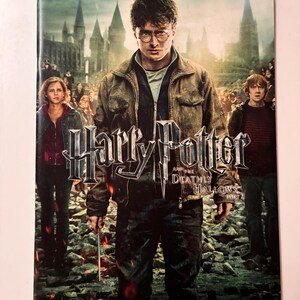 May include: A book cover for "Harry Potter and the Deathly Hallows Part 2" featuring Harry Potter, Hermione Granger, and Ron Weasley. The cover has a dark, dramatic color scheme with a castle in the background.