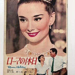 May include: A vintage movie poster featuring Audrey Hepburn in a tiara and a white dress. The poster is for the film "Roman Holiday" and features the text "Roman Holiday" in English and Japanese. The poster also features the text "Audrey Hepburn" in Japanese.
