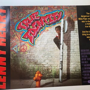 以下が含まれることがあります： レニー・ヘンリー主演の映画「トゥルー・アイデンティティ」のポスター。ポスターには、落書きで覆われたレンガの壁に、映画のタイトルが太字の赤い文字で書かれている。若い男性が白い柱の後ろから覗き込み、手前に消火栓がある。