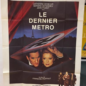 Puede incluir: Un cartel de película vintage de "Le Dernier Métro" con Catherine Deneuve y Gérard Depardieu. El cartel tiene un esquema de color oscuro con el título en letras blancas grandes. La Torre Eiffel es visible en el fondo.