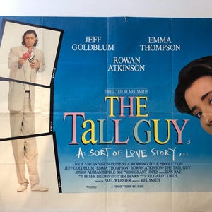 Op de afbeelding: Een filmposter voor de film "The Tall Guy" met Jeff Goldblum, Emma Thompson en Rowan Atkinson. De poster heeft een blauwe achtergrond met de titel in grote, kleurrijke letters. De namen van de acteurs staan onder de titel, samen met de naam van de regisseur, Mel Smith.