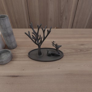 May include: Black metal ring holder shaped like a tree with a deer figurine on a black oval base.