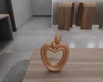 May include: A gold-colored metal sculpture of two figures embracing in the shape of a heart. The sculpture is on a wooden surface.