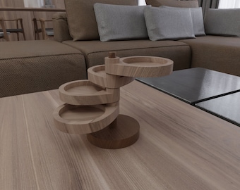 May include: A wooden tiered stand with four circular trays. The stand is made of light brown wood and has a dark brown base. The stand is on a light brown wooden surface.