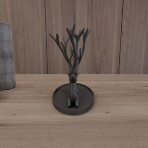 May include: Black deer ring holder with antlers. The deer is sitting on a black circular base.