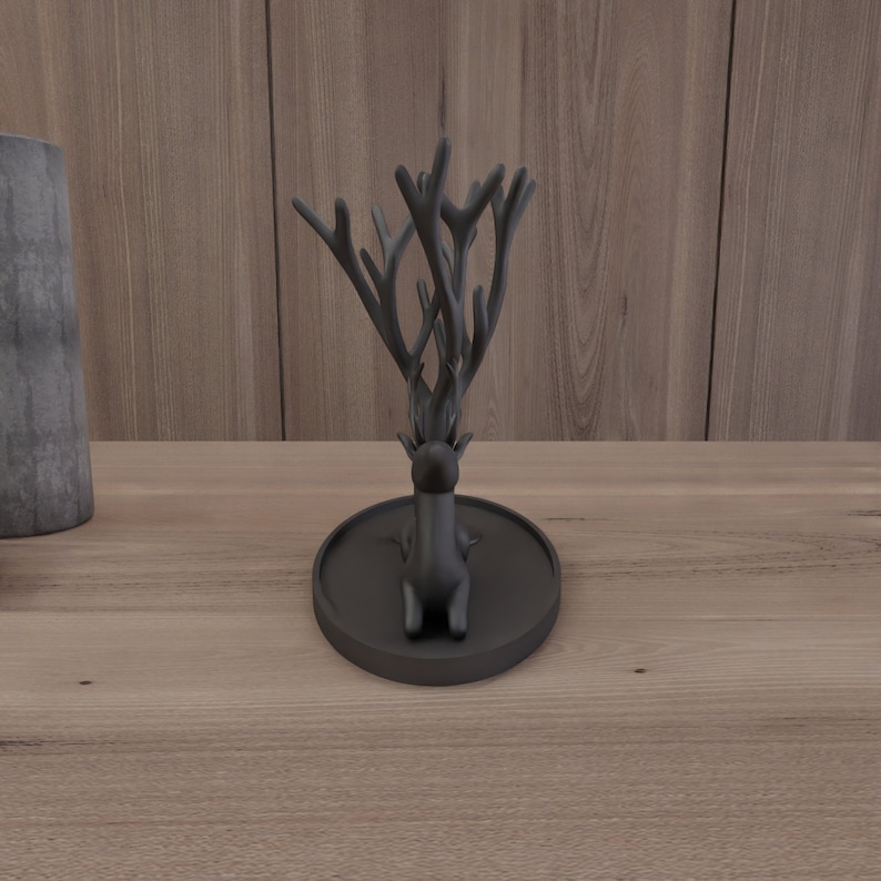May include: Black deer ring holder with antlers. The deer is sitting on a black circular base.