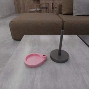 May include: A pink and black ceramic tray set with a round, shallow dish and a tall, cylindrical stand. The tray set is on a gray, textured surface.