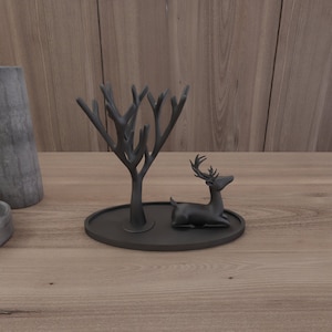 May include: Black metal decorative tray featuring a tree and deer figurine. The tray is round and has a smooth surface.