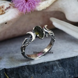 Puede incluir: Un anillo de plata con una piedra preciosa verde y dos lunas crecientes. El anillo está decorado con un diseño de hojas.