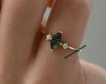 May include: Gold ring with a crescent moon shaped green gemstone and two small clear gemstones. The ring is on a finger.
