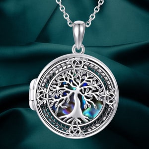 May include: Silver pendant necklace with a round locket showcasing a tree of life design. The tree is set against an iridescent backdrop, framed by Celtic knotwork. The necklace is suspended from a fine chain.