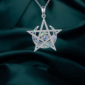 Puede incluir: Collar con colgante plateado con un diseño de pentagrama, que incorpora una luna creciente y un motivo circular central. El colgante presenta una incrustación de nácar con tonos azules, verdes y dorados, suspendido de una fina cadena.