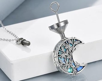 May include: A silver crescent moon pendant necklace with a tree of life design. The pendant is made of metal and has a blue and green abalone shell inlay. The necklace is attached to a silver chain.