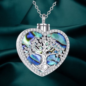 May include: Silver-toned heart-shaped pendant necklace. The pendant features a tree of life design with a mother-of-pearl inlay in shades of blue and green. The pendant is encrusted with small, clear crystals and hangs from a delicate chain.