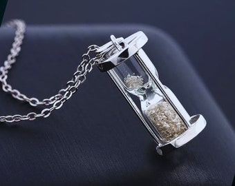 May include: A silver chain necklace with a silver hourglass pendant. The hourglass is filled with silver glitter.