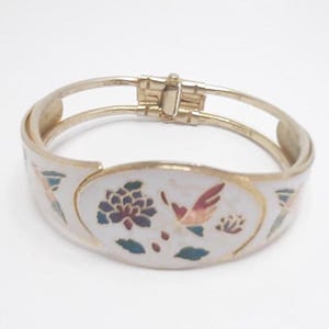 Op de afbeelding: Een witte emaille armband met een gouden afwerking. De armband heeft een bloemen- en vogelontwerp in tinten blauw, roze, groen en geel.