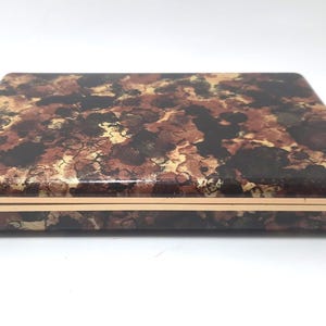 May include: A rectangular box with a marbled pattern in shades of brown, gold, and black. The box has a gold-colored trim around the edges. The lid and sides have a glossy finish.