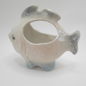 May include: A white ceramic fish planter with a textured surface and blue accents. The fish has a hole in the middle for planting.
