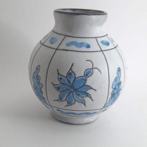 Könnte beinhalten: Eine weiße Keramikvase mit rundem Körper und schmalem Hals. Die Vase ist mit blauen floralen und geometrischen Mustern verziert. Der Rand ist dunkelgrau.