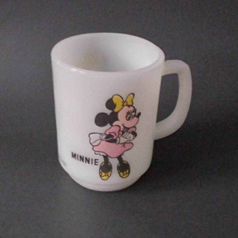 May include: White ceramic mug with a cartoon image of Minnie Mouse wearing a pink dress and yellow bow. The mug says "MINNIE" at the bottom.