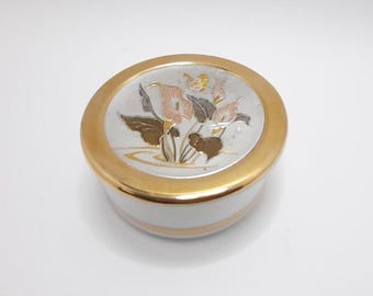 Könnte beinhalten: Eine weiße Porzellan-Schmuckdose mit goldfarbenem Rand und einem silbernen und goldenen Blumendesign auf dem Deckel. Das Design zeigt rosa Blumen, grüne Blätter und einen goldenen Schmetterling.